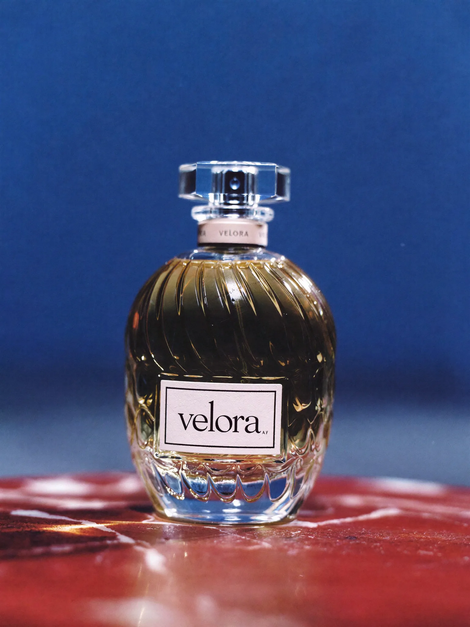 Velora fragrance on a reflective red surface against blue
